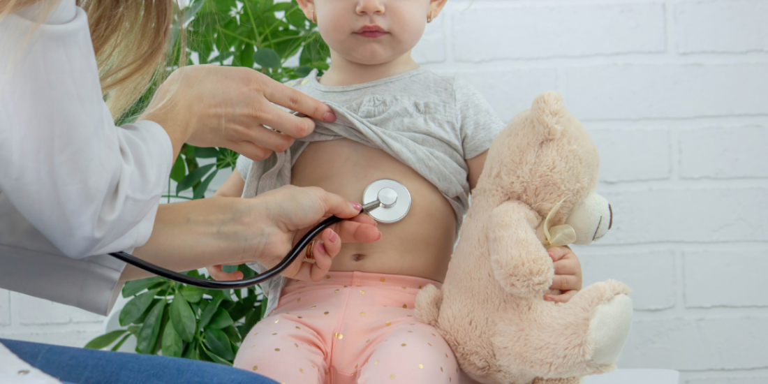 A young girl holding her teddy bear with her GP checking her chest with a stethoscope