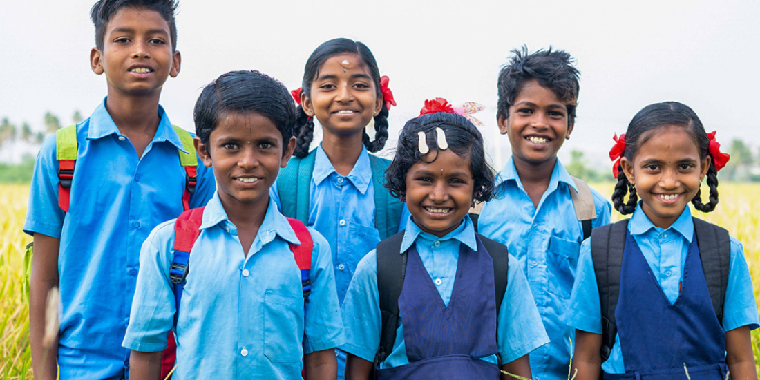 Boys and girls with backpacks and in school uniform line up for the camera.