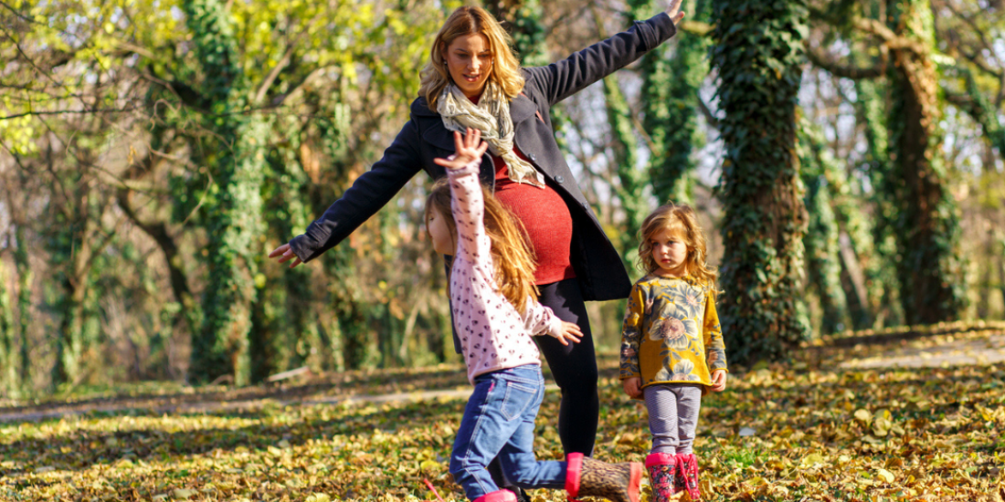 Pregnant mother enjoying with her two daughters in park on sunny autumn day.