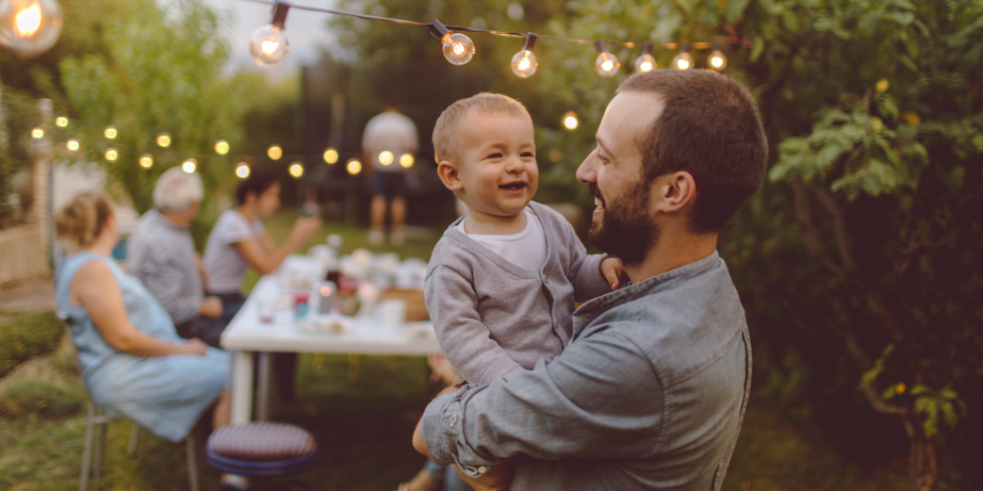 A father holding his child with multigenerational family in the background